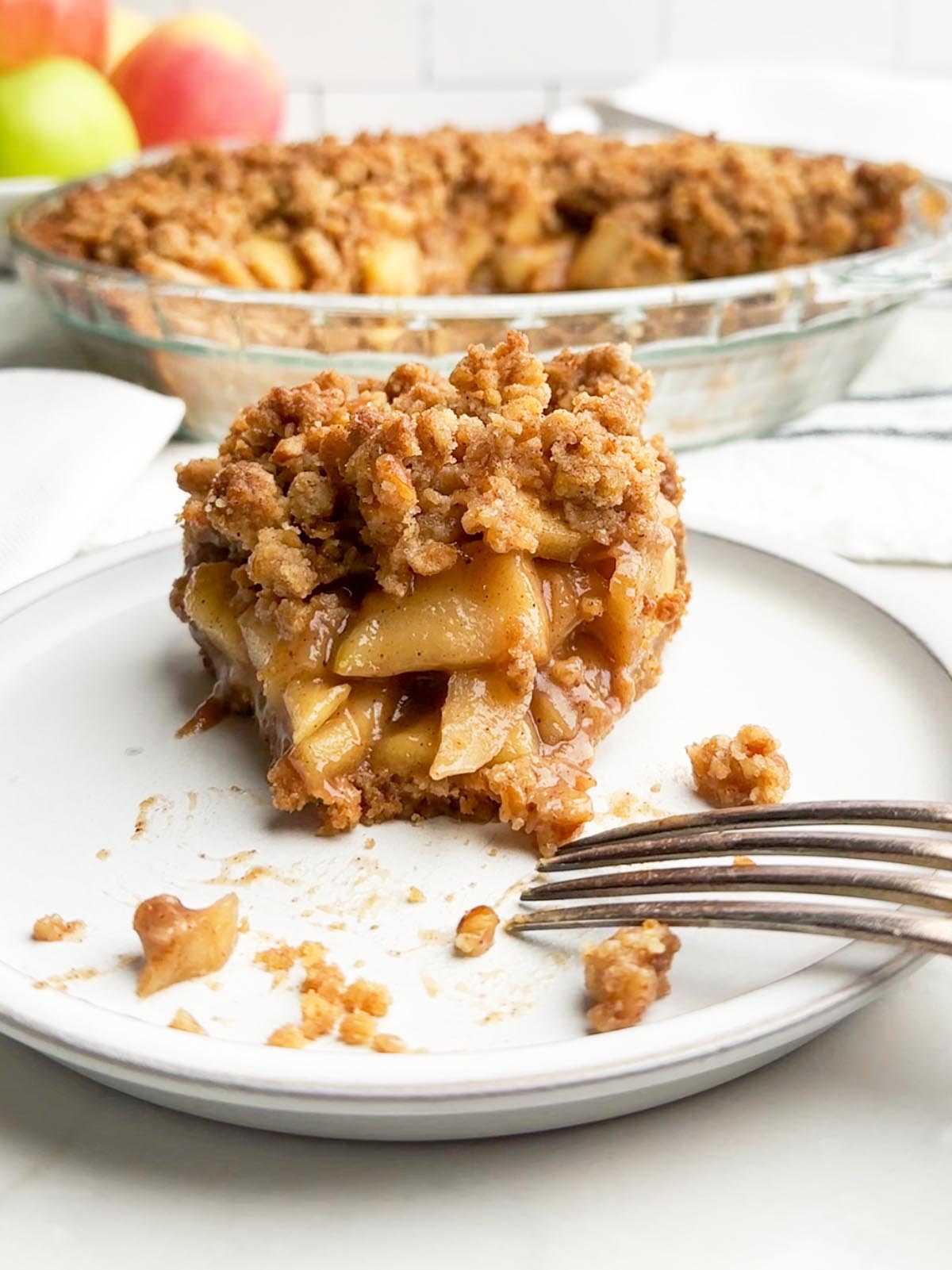 half eaten piece of apple pie with graham cracker crust on a white plate.