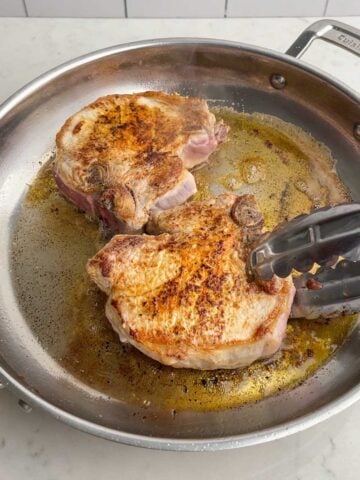 browned pork chops in stainless steel skillet.
