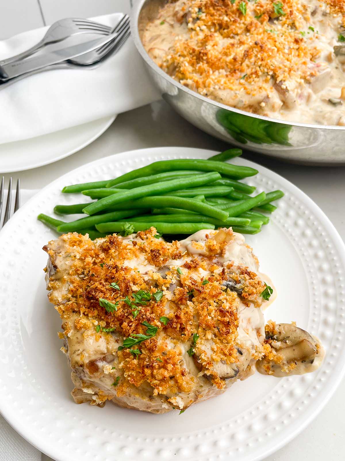 baked pork chops with cream of mushroom soup on a white plate with green beans.