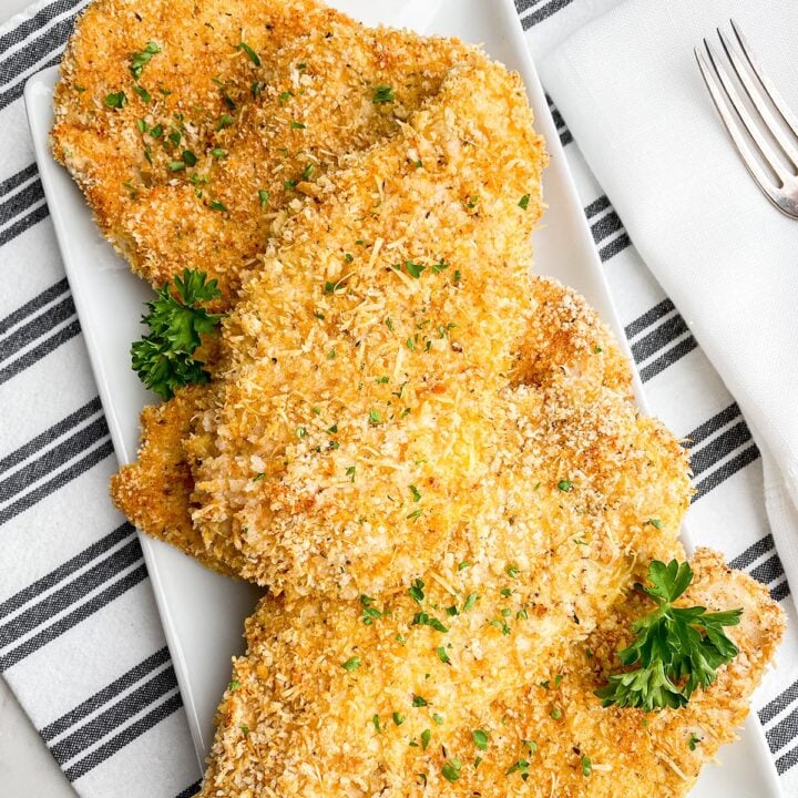 baked thin sliced chicken with panko on white platter on black and white napkin