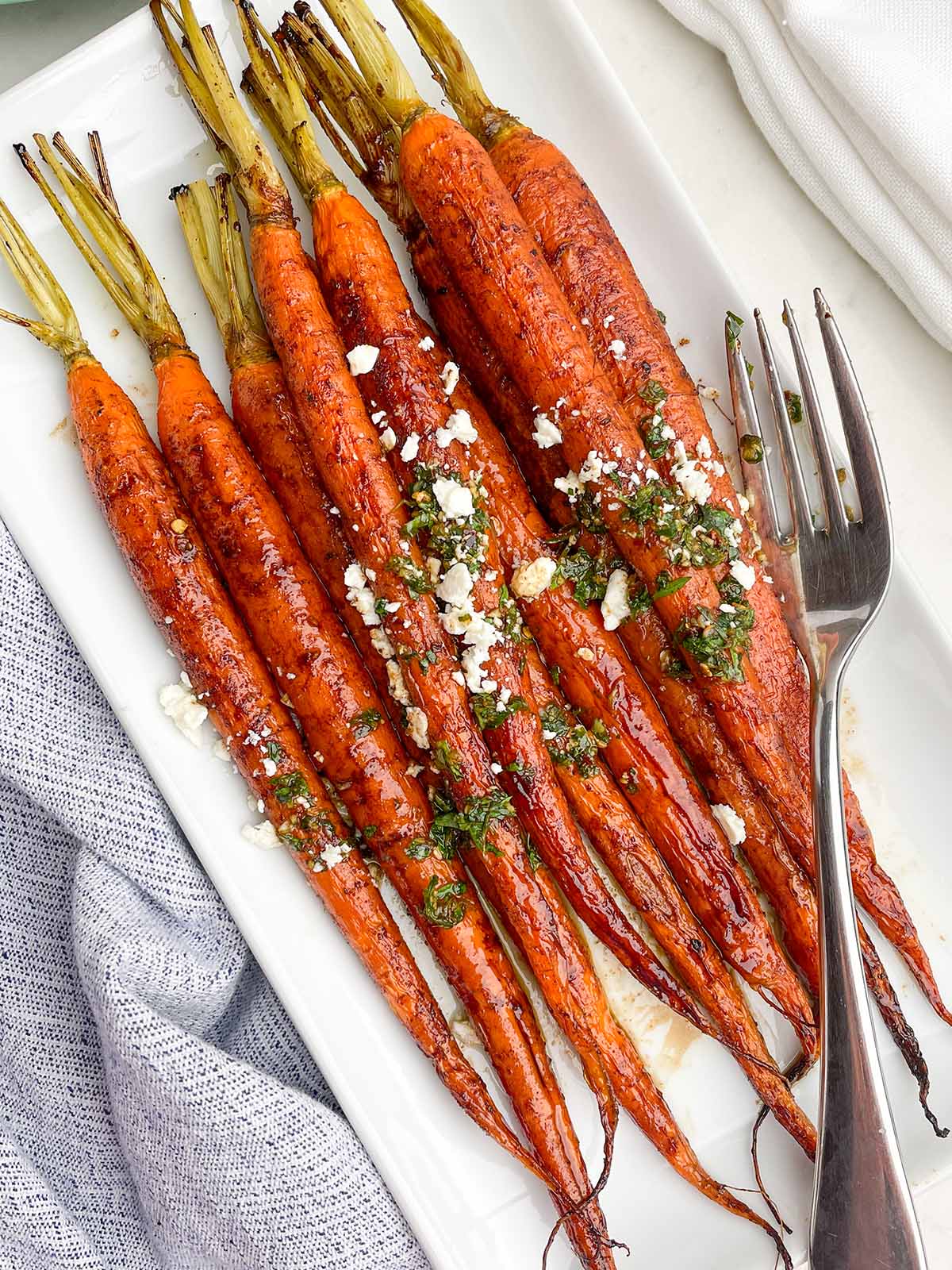 maple balsamic glazed carrots topped with feta and chimichurri on a white platter.