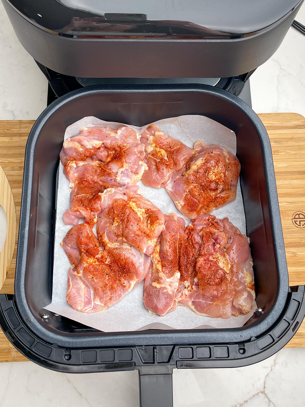 uncooked boneless skinless chicken thighs on parchment in air fryer