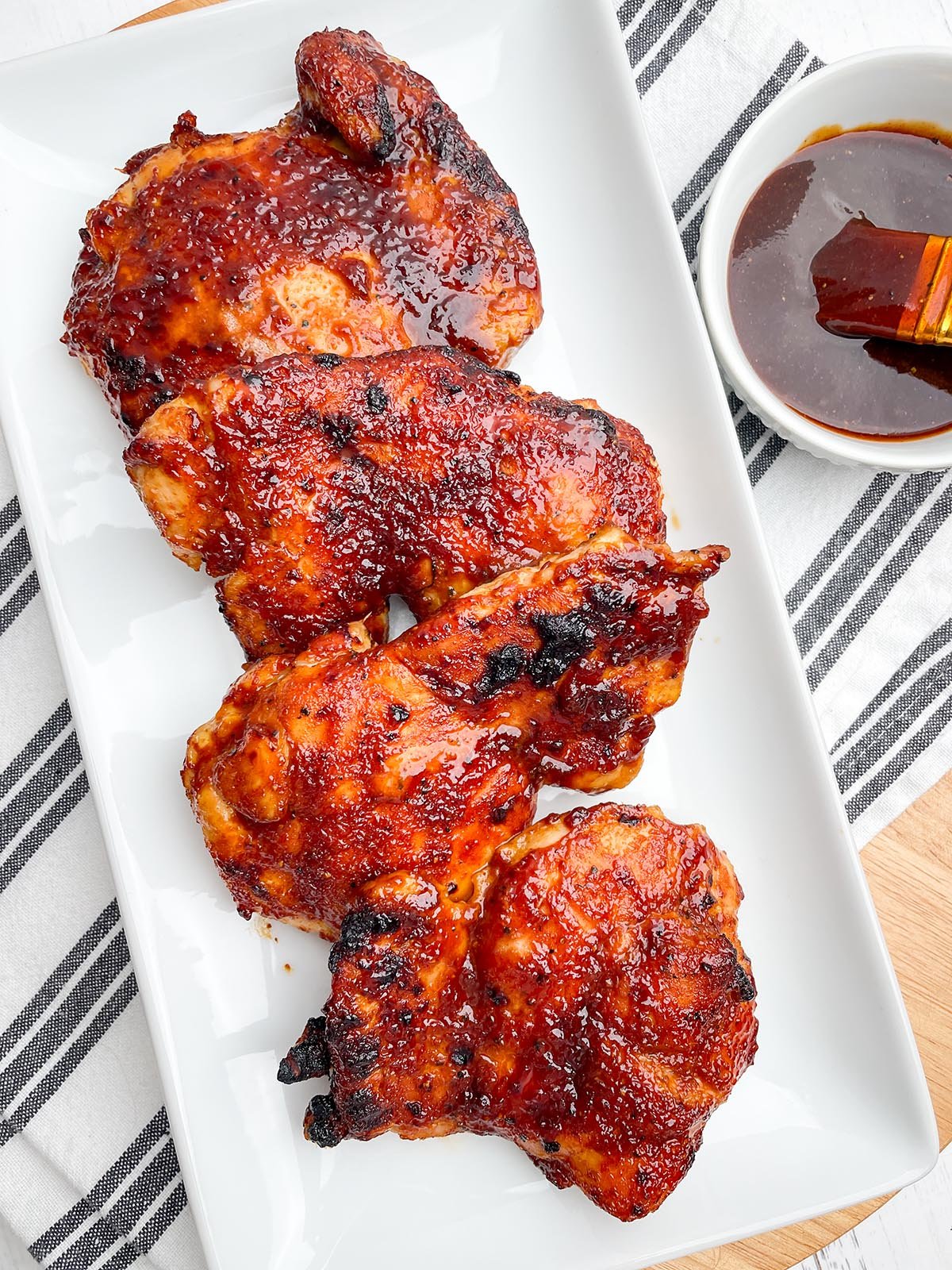 air fryer bbq chicken thighs on a white platter next to bowl of bbq sauce