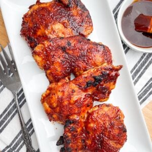 air fryer bbq chicken thighs on a white platter next to bowl of bbq sauce