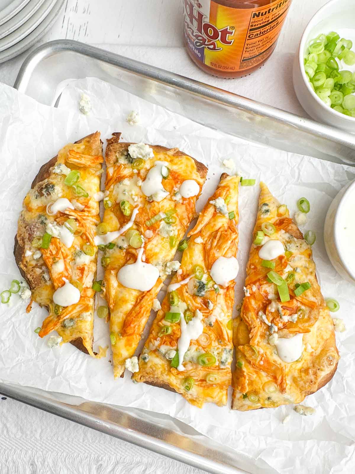 slices of buffalo chicken flatbread on a baking sheet lined with parchment paper