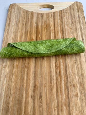 Rolled up Chicken Cranberry Salad Pinwheel on a wooden cutting board. 