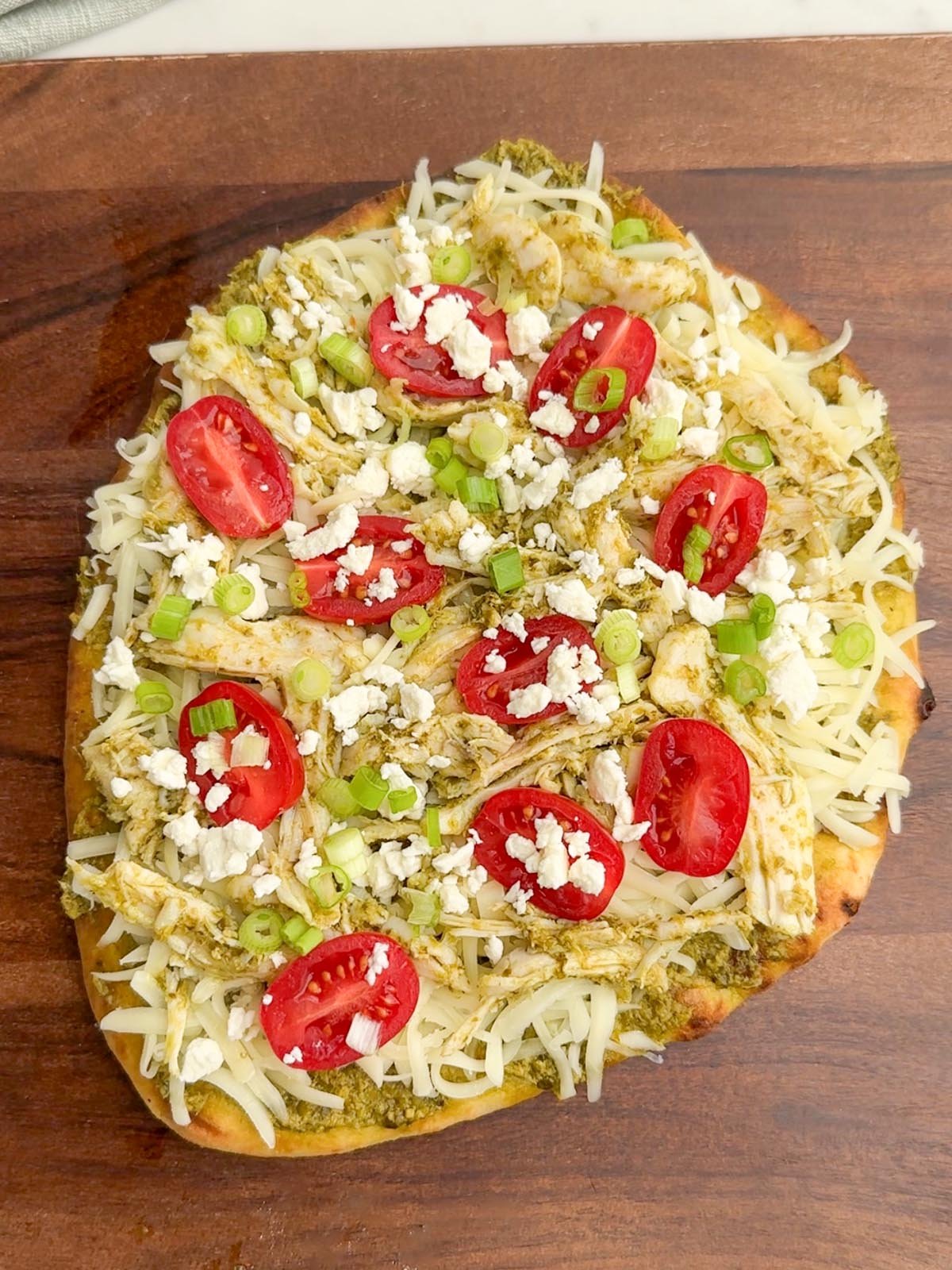 unbaked pesto chicken flatbread on a wooden cutting board