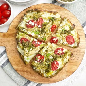 chicken pesto flatbread cut into 4 pieces on a round wooden cutting board