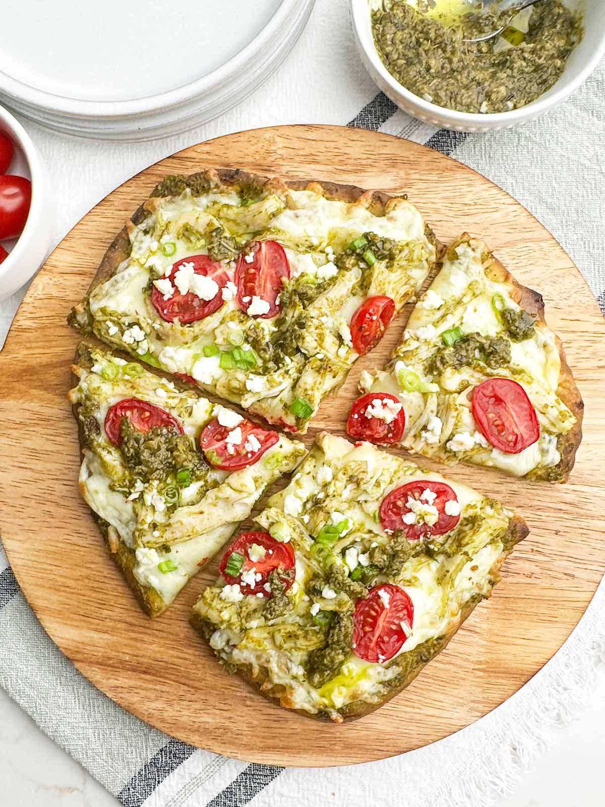 chicken pesto flatbread cut into 4 pieces on a round wooden cutting board