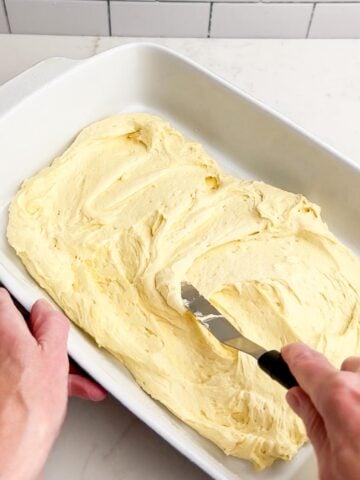 hand holding a spatula spreading cake batter in a baking pan.