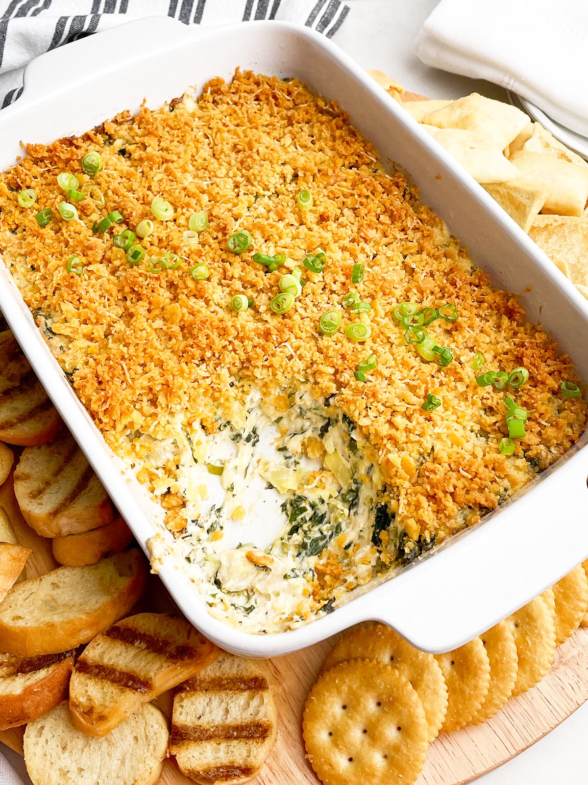 crab spinach artichoke dip in white baking dish with pita chips and crostini.