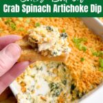 hand holding crostini with crab spinach artichoke dip on top with baking dish of dip in background