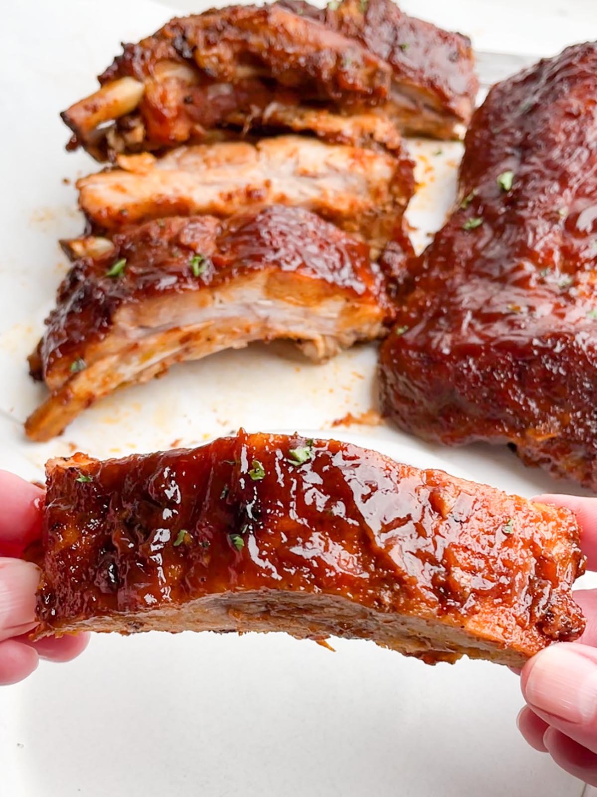 hands holding one rib in foreground with racks of ribs in the background