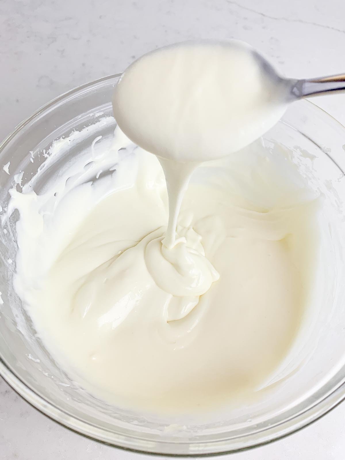 white chocolate cream cheese frosting in clear bowl with spoon