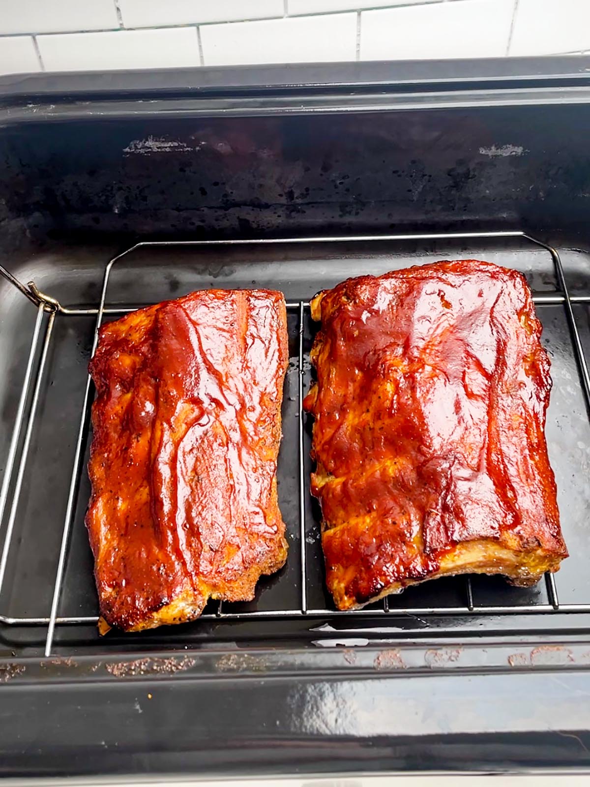 two cooked racks of ribs in a black roaster oven pan