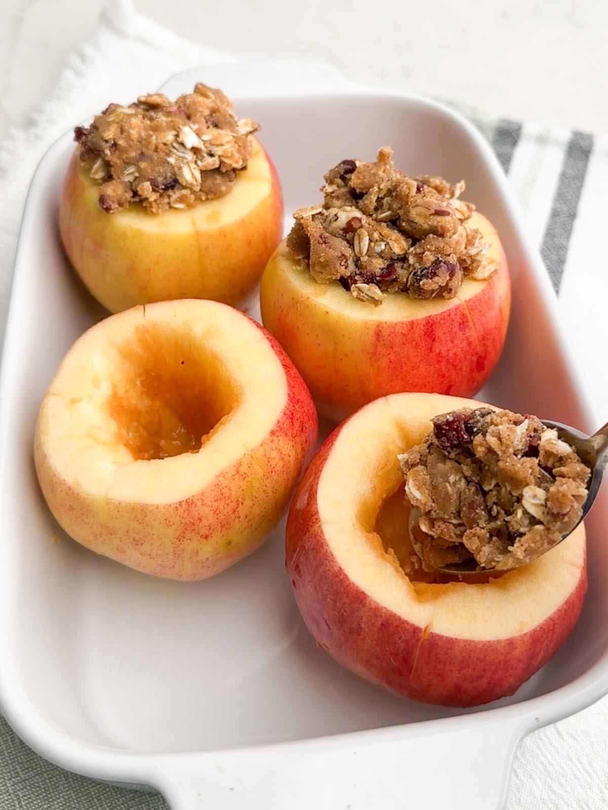 spoon dropping crumble mixture into cored apple