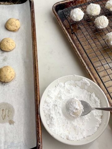 spoon lifting a rolled Mexican Christmas cookie out of a bowl of powdered sugar.