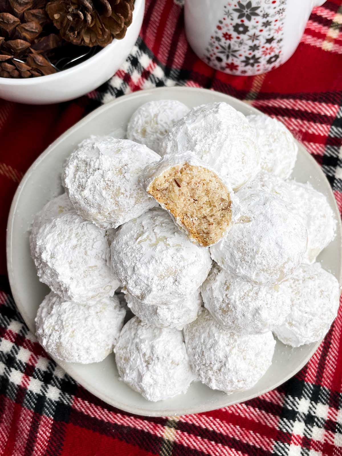 Mexican Christmas cookies on a white plate next to a holiday mug and bowl of pine cones.