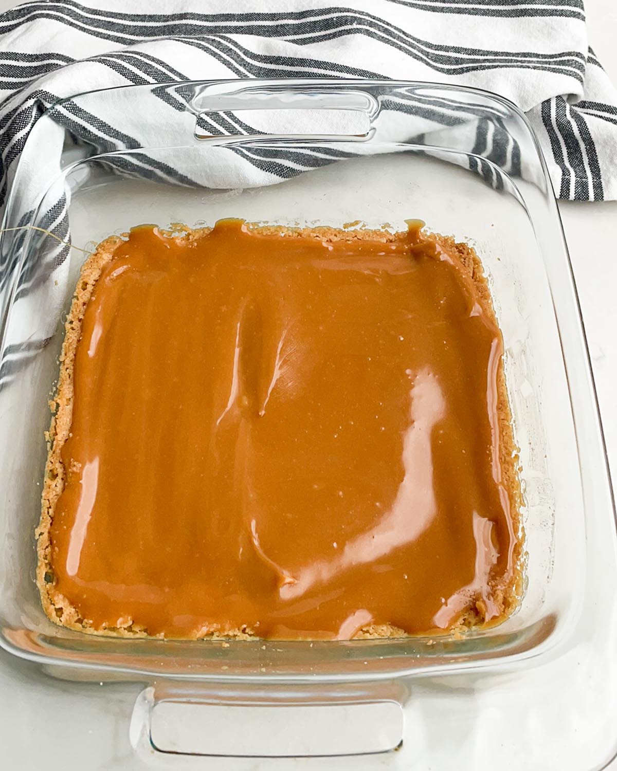 Shortbread crust with caramel poured over the top in a clear baking dish