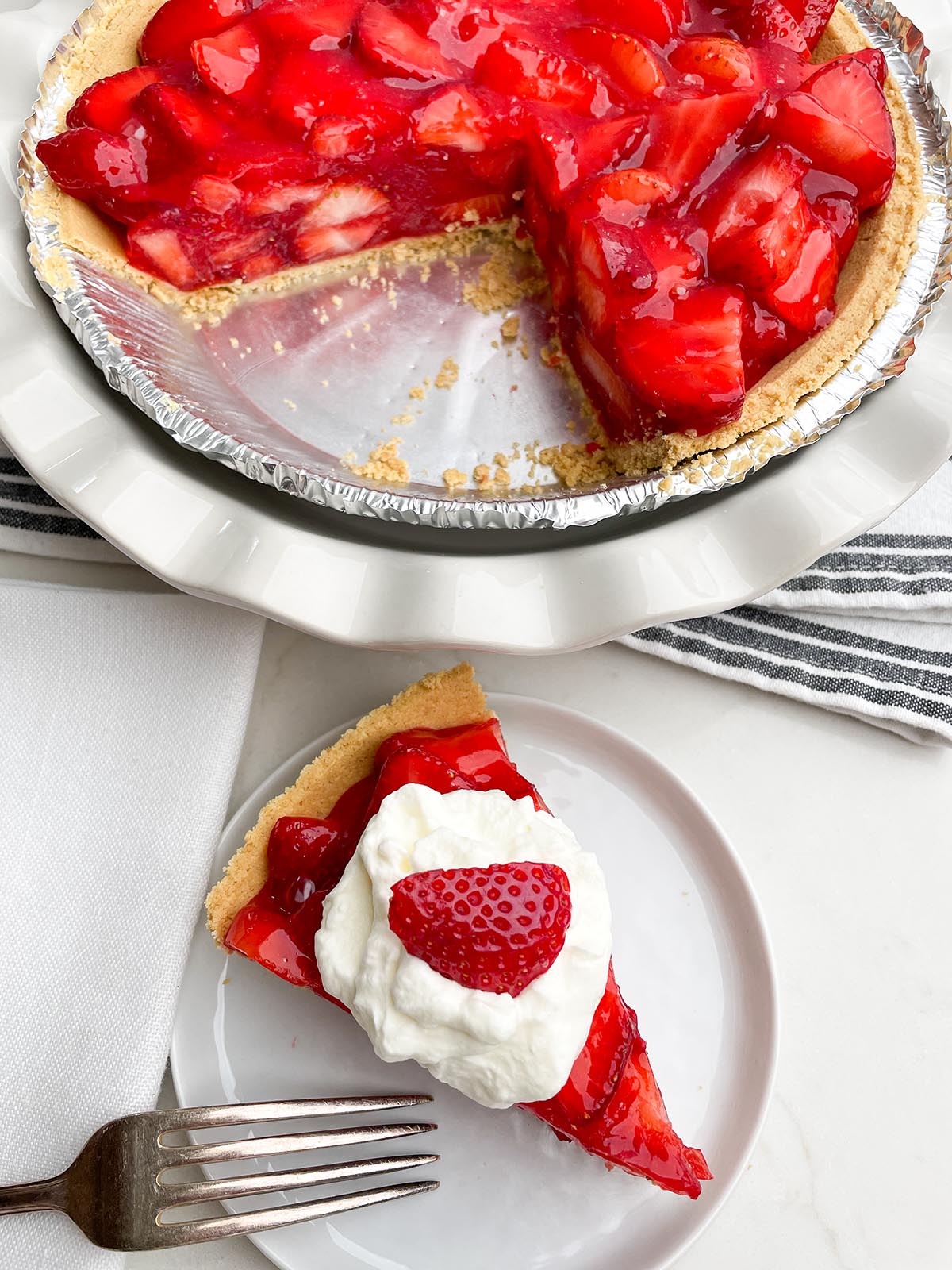 piece of strawberry pie in a white plate next to strawberry pie in white pie plate.