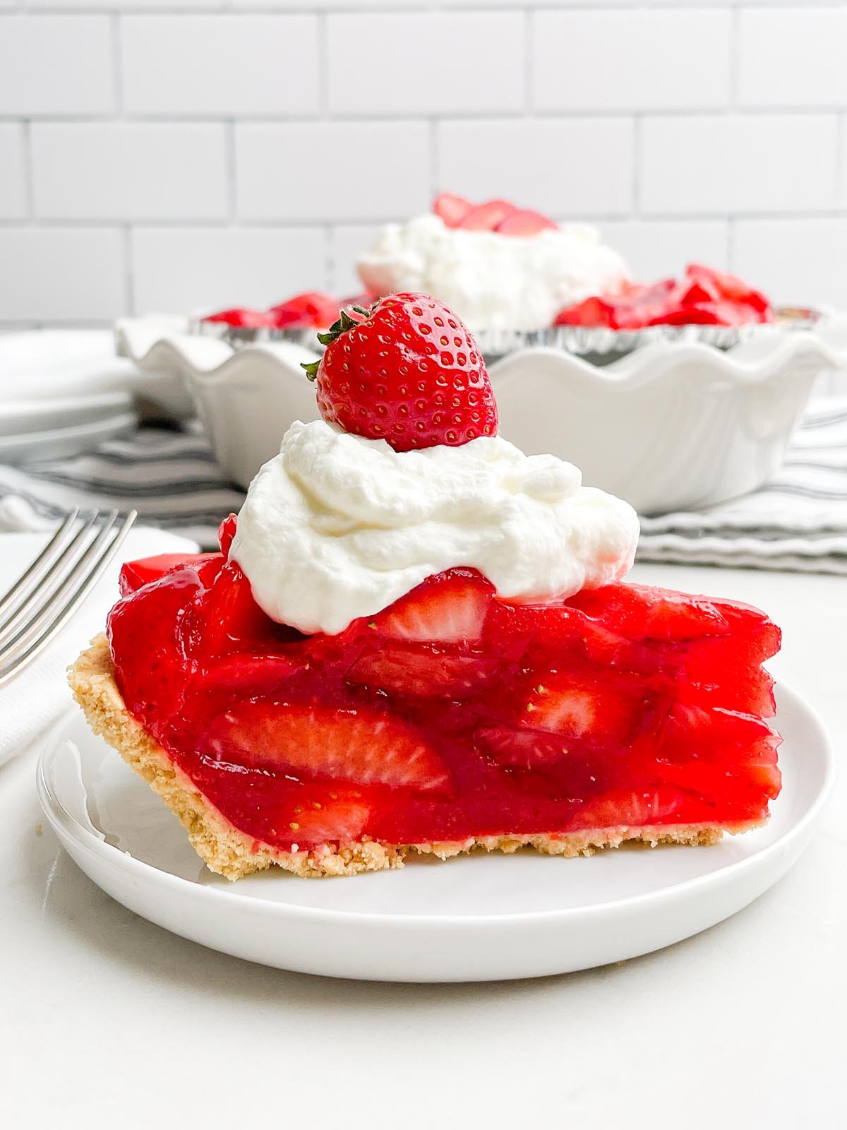 side view of piece of strawberry pie topped with whipped cream and a strawberry.