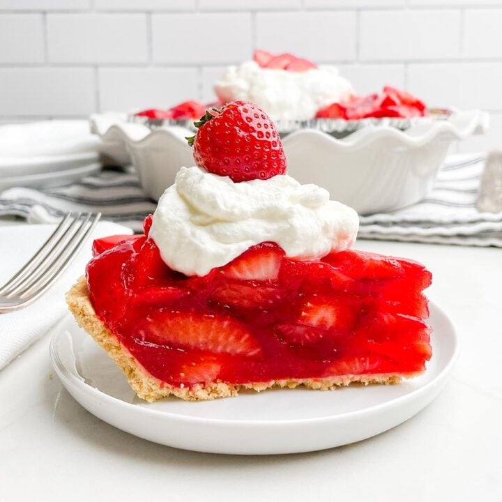 side view of piece of strawberry pie topped with whipped cream and a strawberry