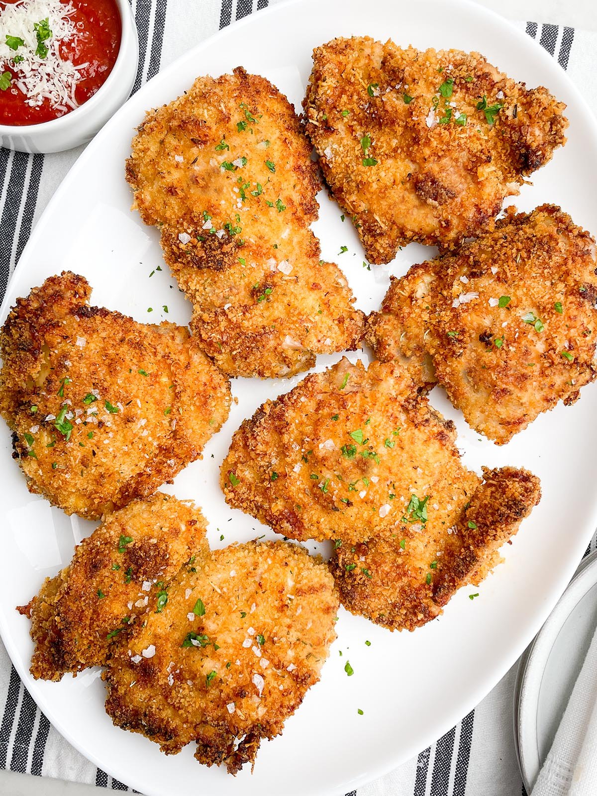 air fryer panko chicken thighs on a white platter next to a bowl of marinara