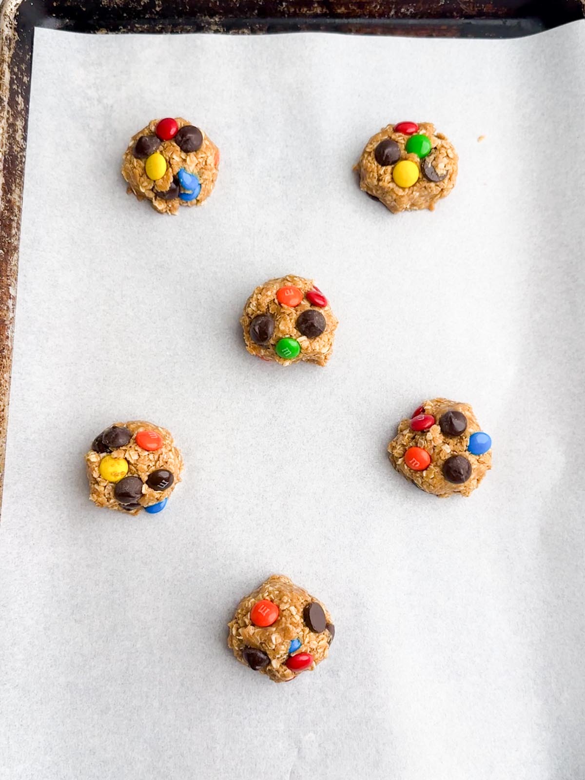 Monster cookie dough balls on parchment paper.