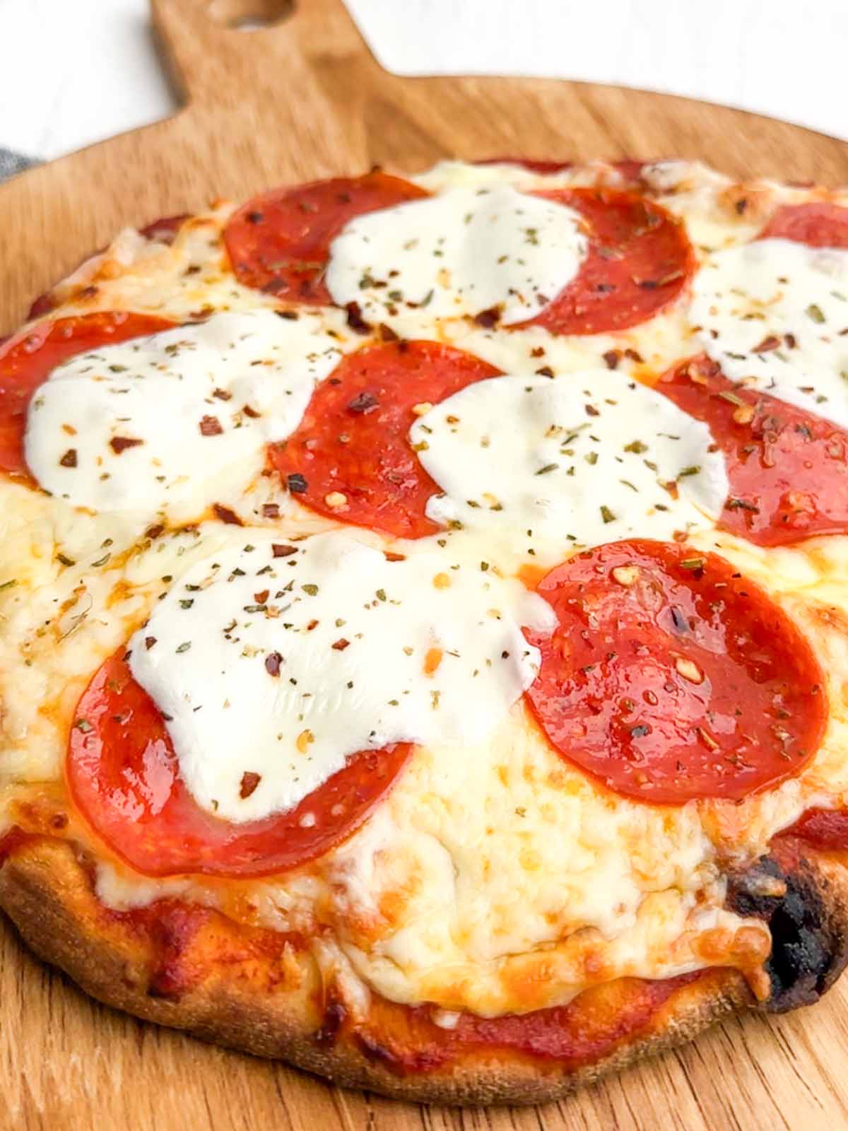 baked pepperoni flatbread on a wooden cutting board