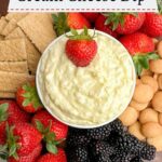 pineapple cream cheese dip in a white bowl on a wooden cutting board with fruit, graham crackers, and cookies