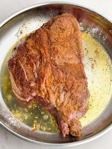 Chuck roast searing in a skillet with olive oil.