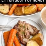pot roast with onion soup mix, potatoes, and carrots on a white plate with platter of pot roast in background