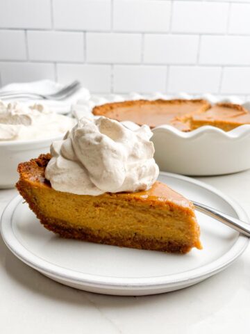 piece of pumpkin pie with graham cracker crust with a dollop of cinnamon brown sugar whipped cream.