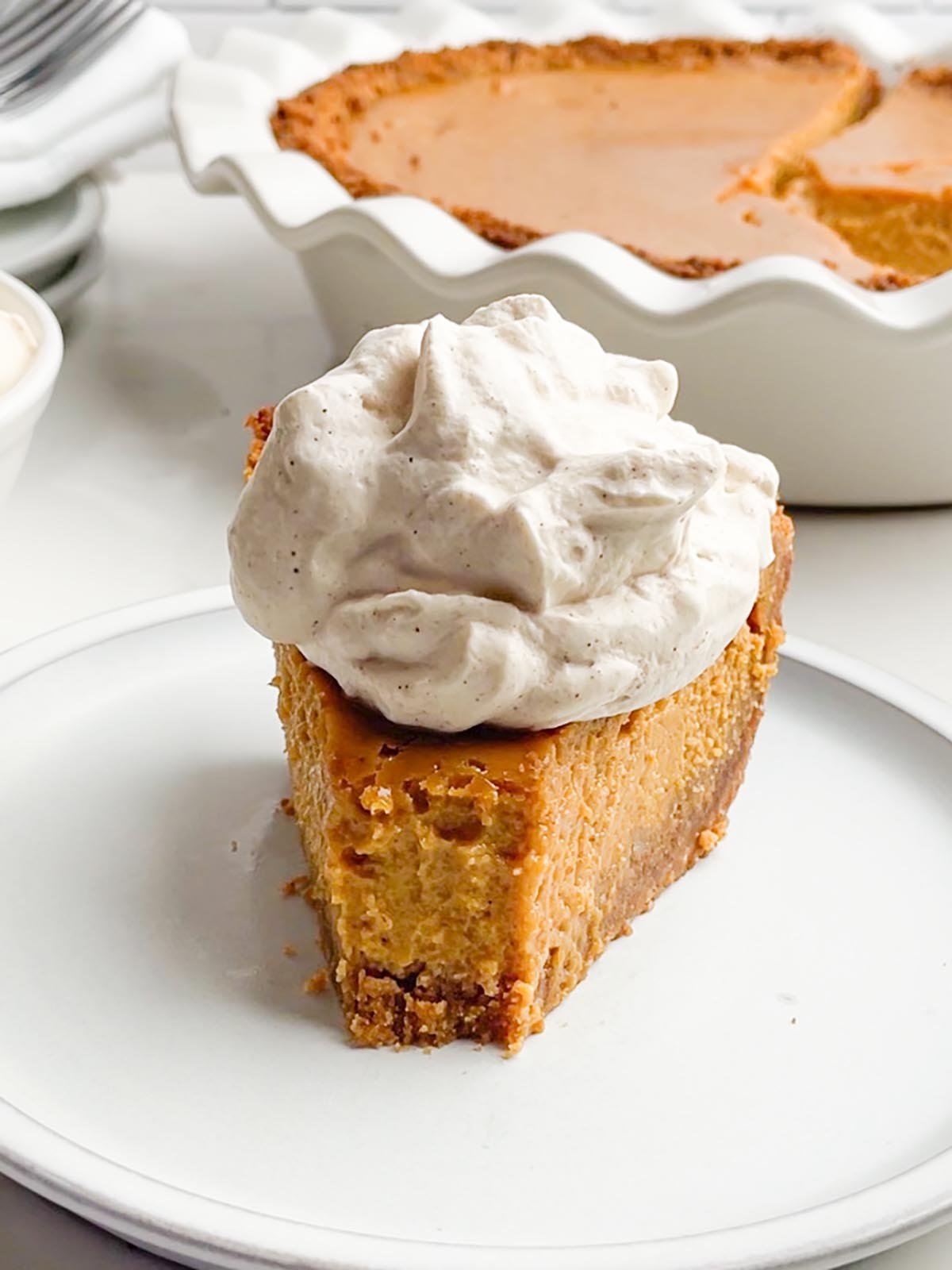 piece of pumpkin pie with graham cracker crust with a dollop of cinnamon brown sugar whipped cream.