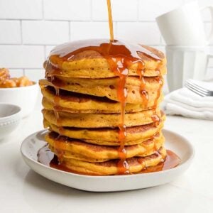 pumpkin syrup being poured onto pumpkin pancakes