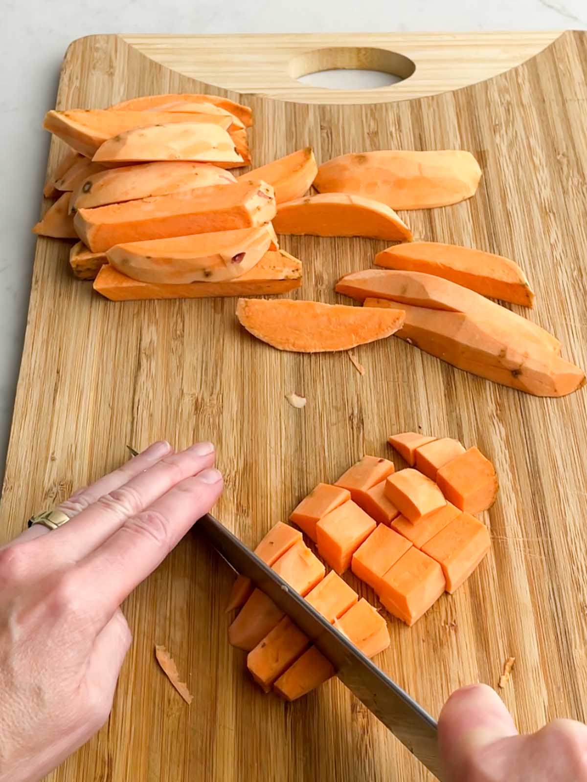 hand on knife cutting sweet potato into cubes