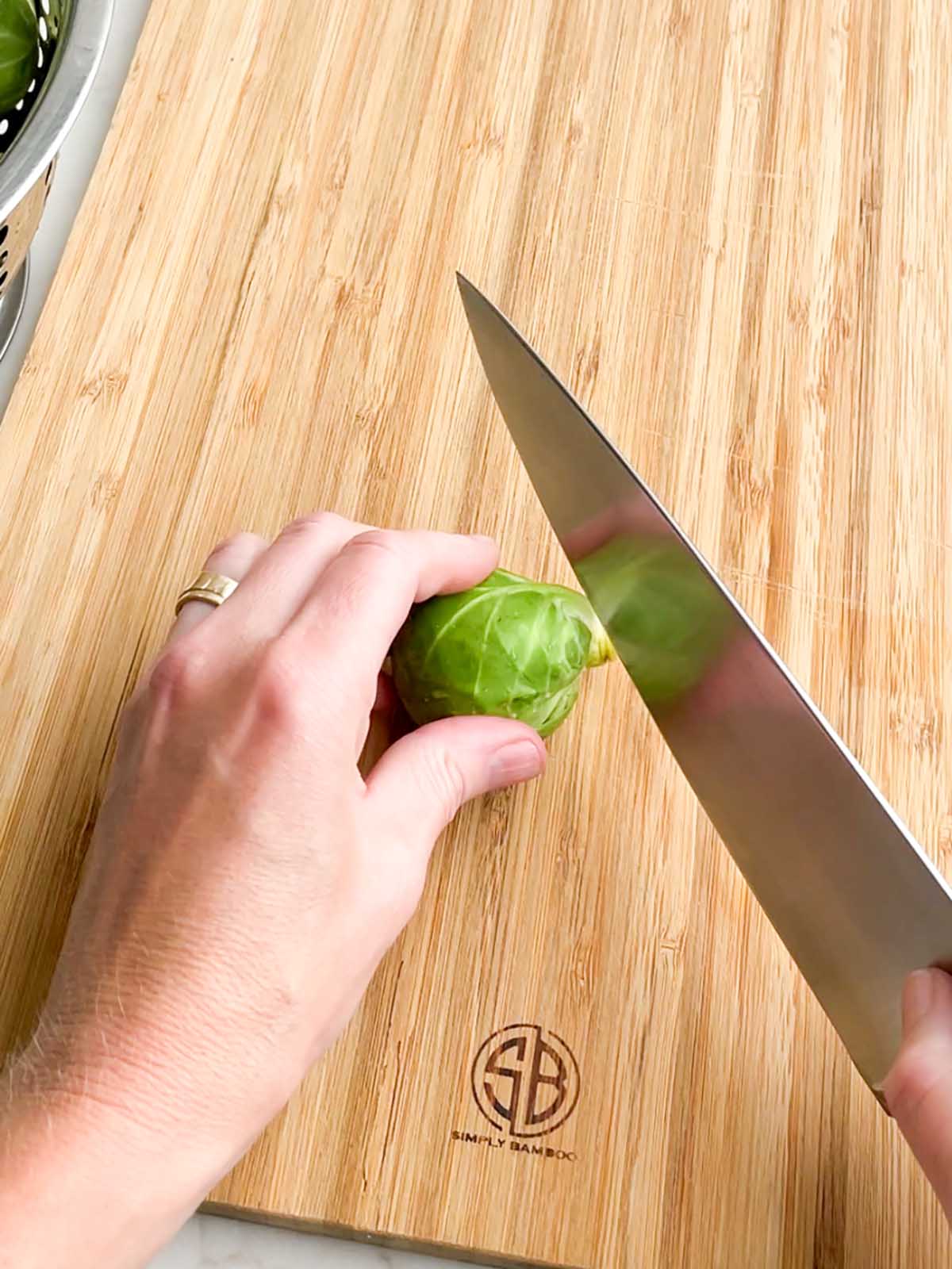 hand holding knife cutting bottom off of brussels sprout