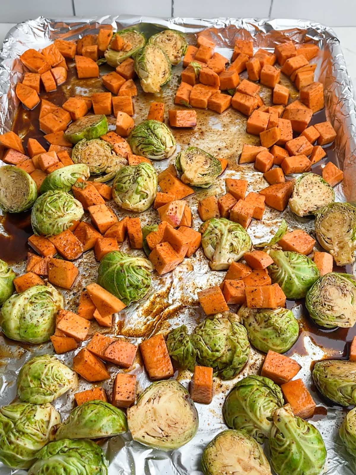raw brussels sprouts and sweet potatoes tossed in maple balsamic dressing on baking sheet
