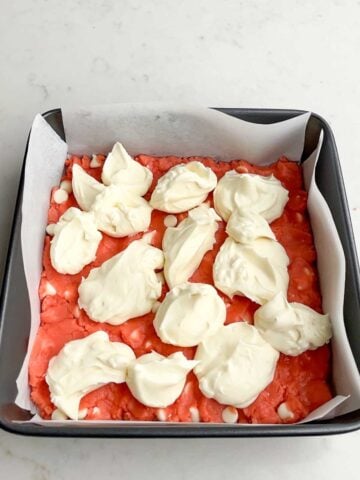 cream cheese dolloped over strawberry brownie batter in a pan.