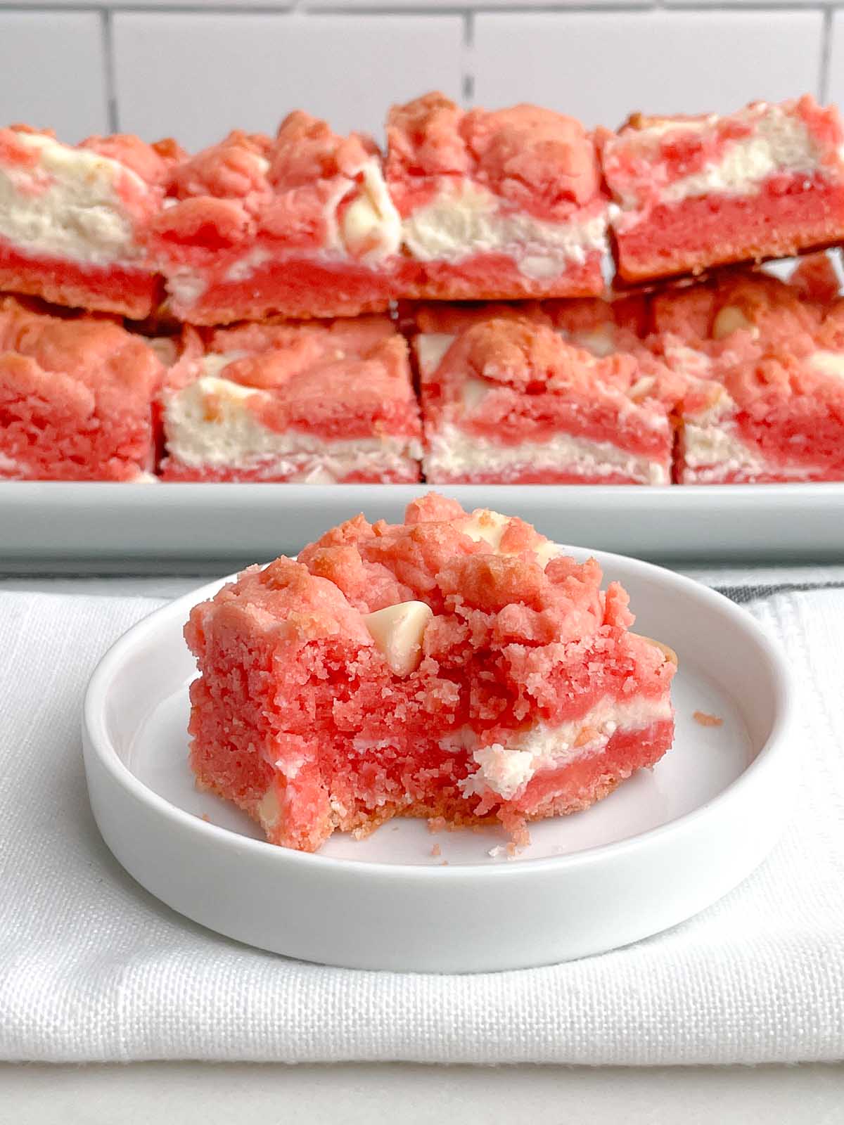 one Strawberry Brownie ona white plate in front of a platter of strawberry brownies.