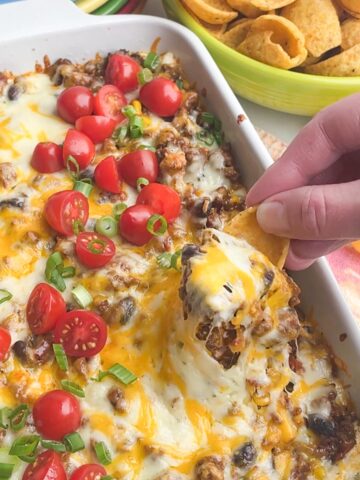hand with chip scooping taco dip.