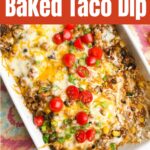 taco dip recipe with ground beef in white casserole dish with colorful napkin, plates, and scoops chips on counter