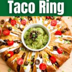 taco ring covered in toppings with guacamole in the center on a wooden cutting board